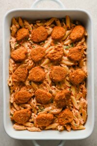 penne pasta with creamy tomato sauce in rectangular baking dish topped with chicken nuggets.