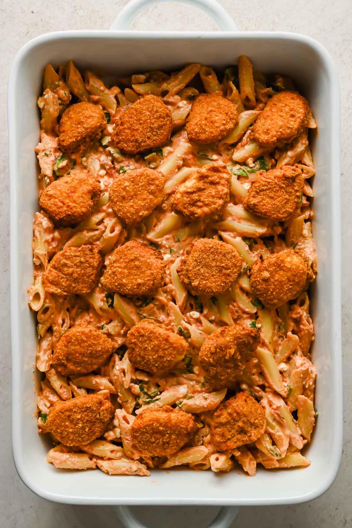 penne pasta with creamy tomato sauce in rectangular baking dish topped with chicken nuggets.