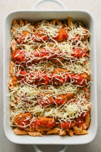 healthier chicken parm bake in rectangular baking dish topped with shredded mozzarella before baking.