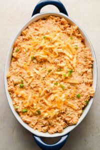 buffalo chicken casserole ingredients in large oval baking dish topped with shredded cheddar.