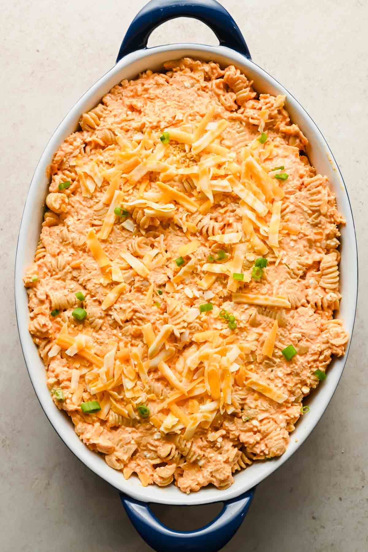 buffalo chicken casserole ingredients in large oval baking dish topped with shredded cheddar.
