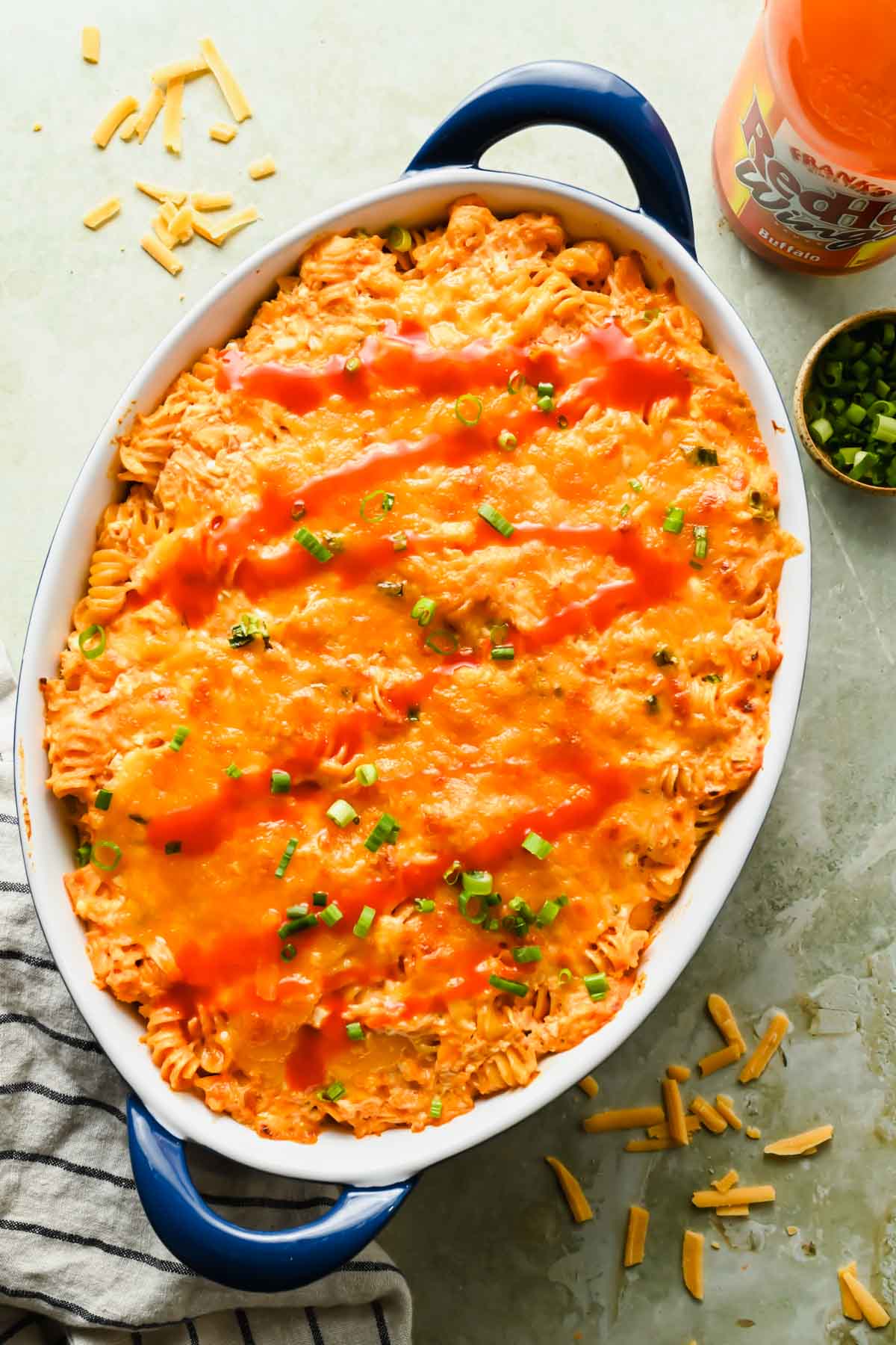 baked buffalo chicken casserole ingredients in large oval baking dish topped with extra buffalo sauce.