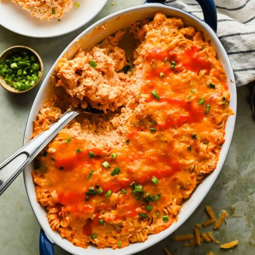 baked buffalo chicken casserole ingredients in large oval baking dish topped with eserving scooped out.