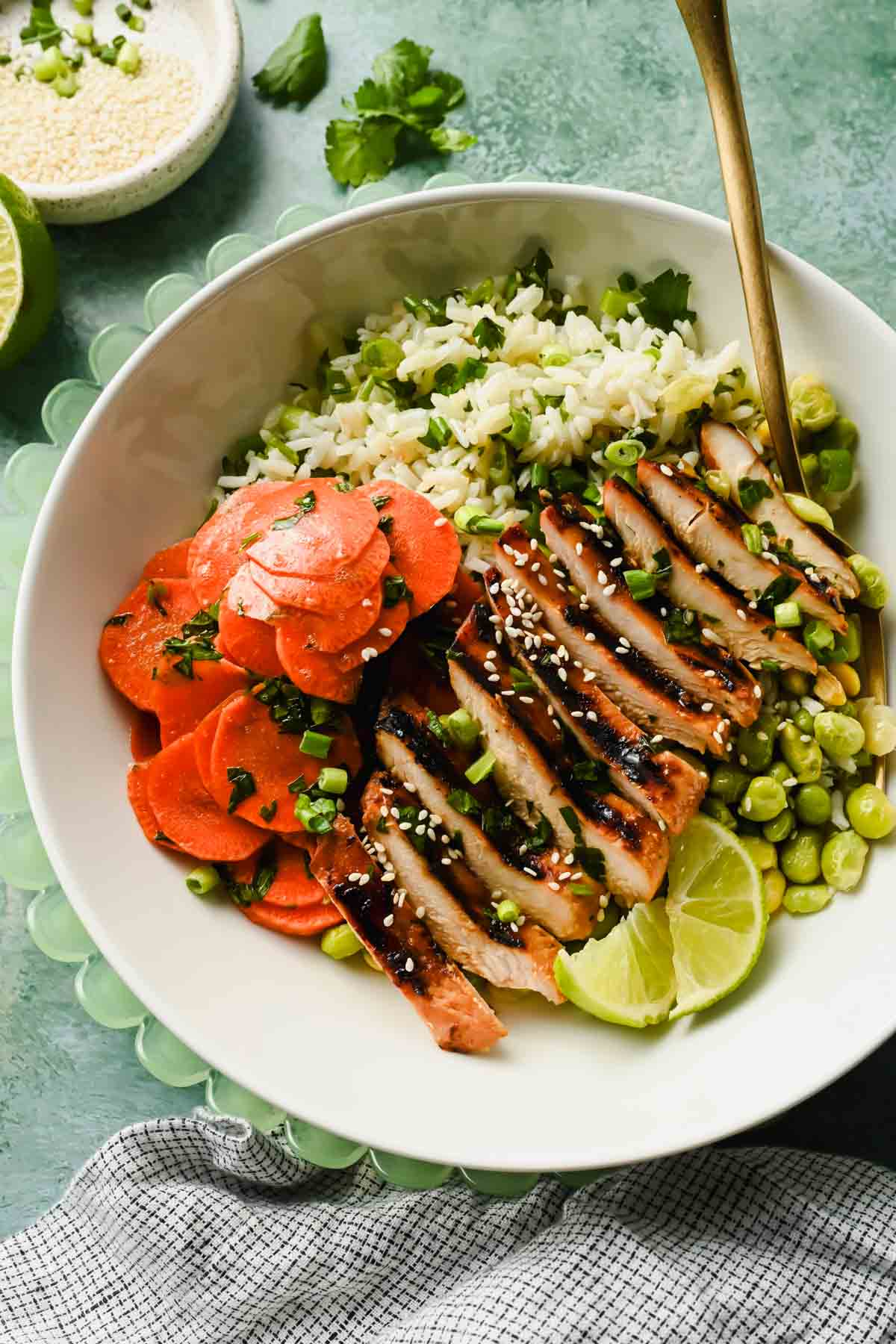 herb rice topped with miso chicken and sliced carrot salad in white serving bowl.