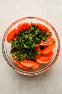 sliced carrots and diced herbs in large glass mixing bowl.