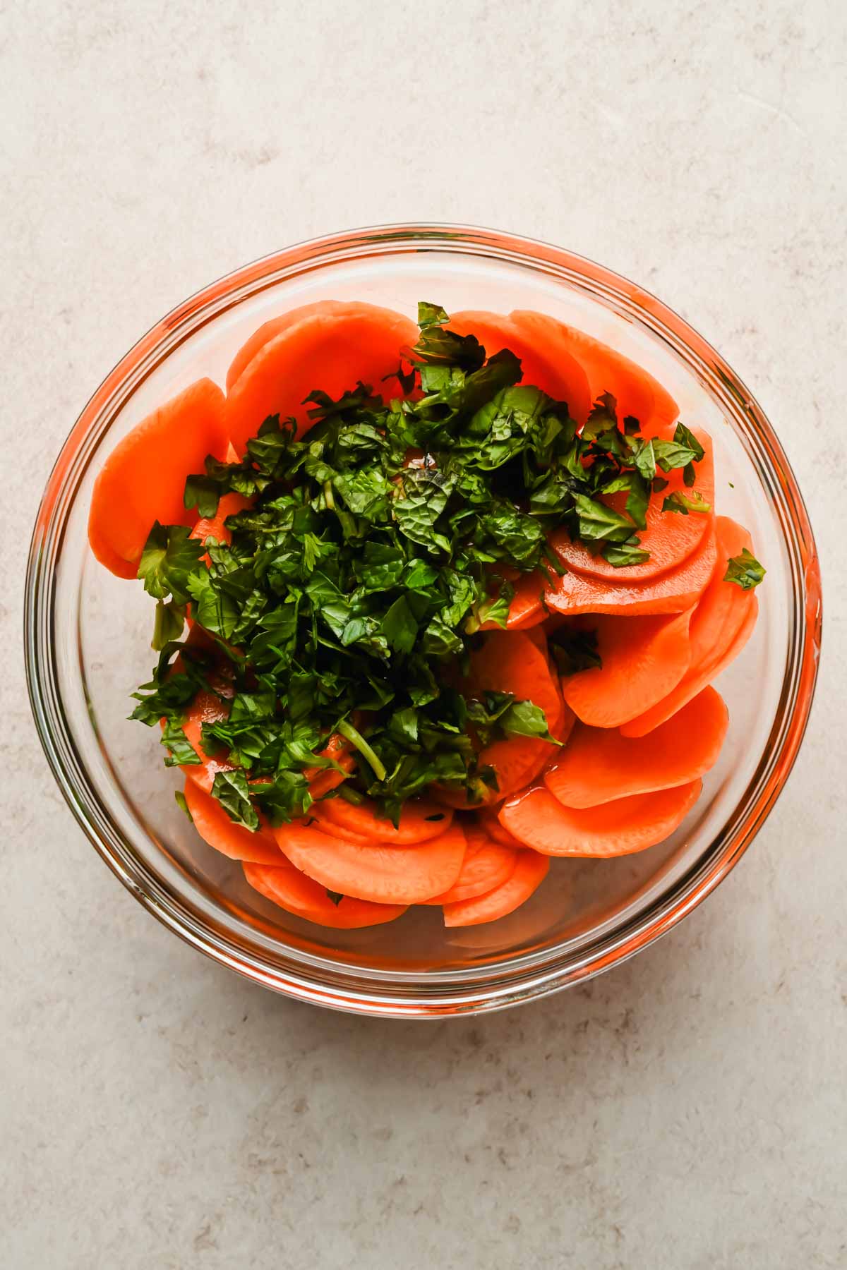 sliced carrots and diced herbs in large glass mixing bowl.