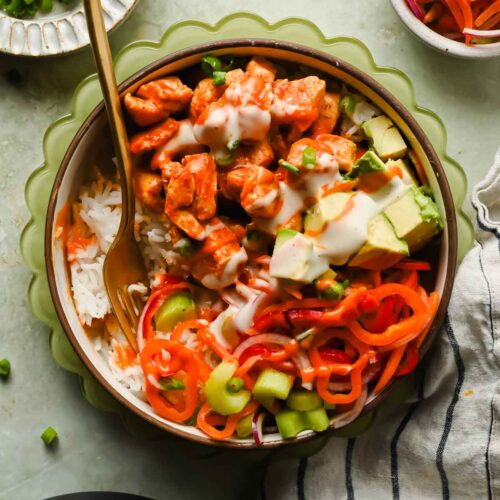 buffalo chicken over rice plated with a bell pepper salad and avocado drizzled with extra buffalo sauce and ranch.