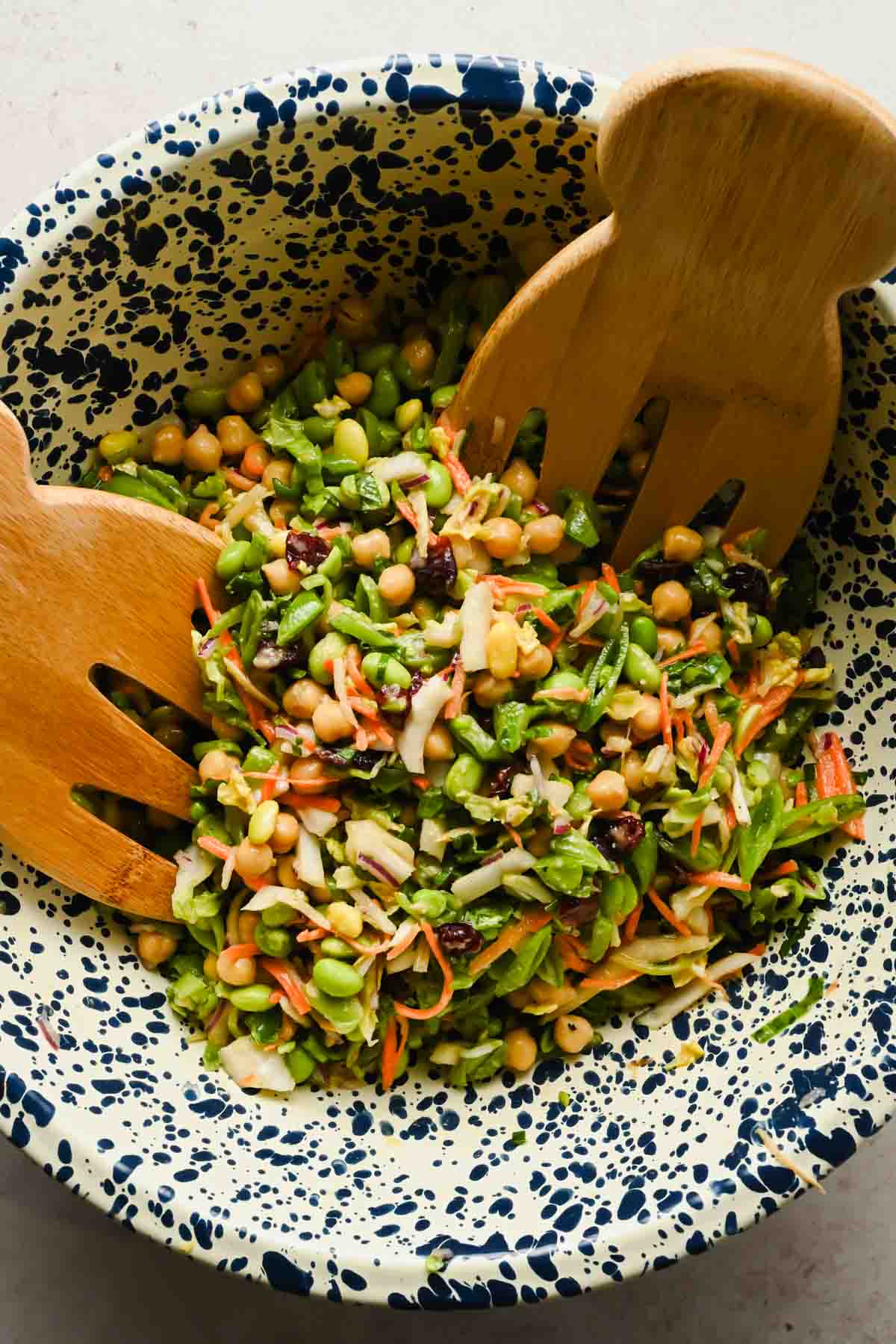 edamame and snap pea and chickpeas salad in large speckled mixing bowl with wooden tongs.