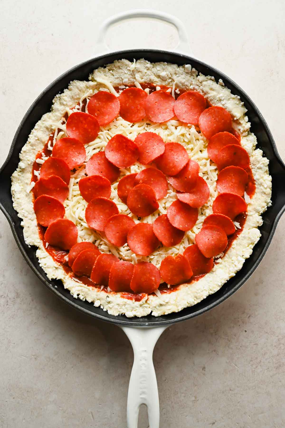 pizza dough pushed into cast iron skillet topped with marinara, cheese and pepperonis.