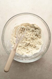 pizza crust ingredients in glass mixing bowl with whisk.
