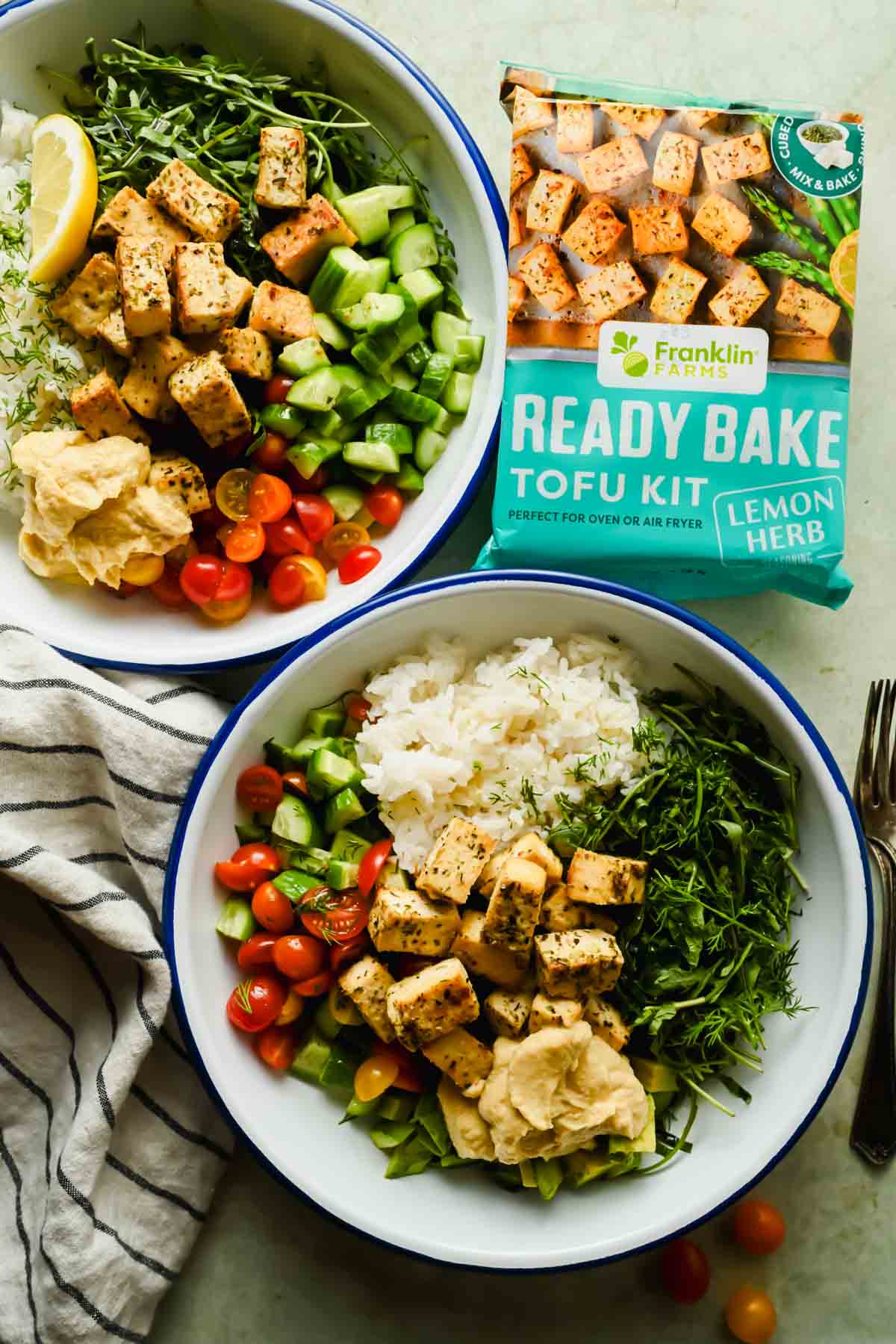 two Mediterranean tofu bowls with herbed rice, cucumber, tomato and a dollop of hummus.
