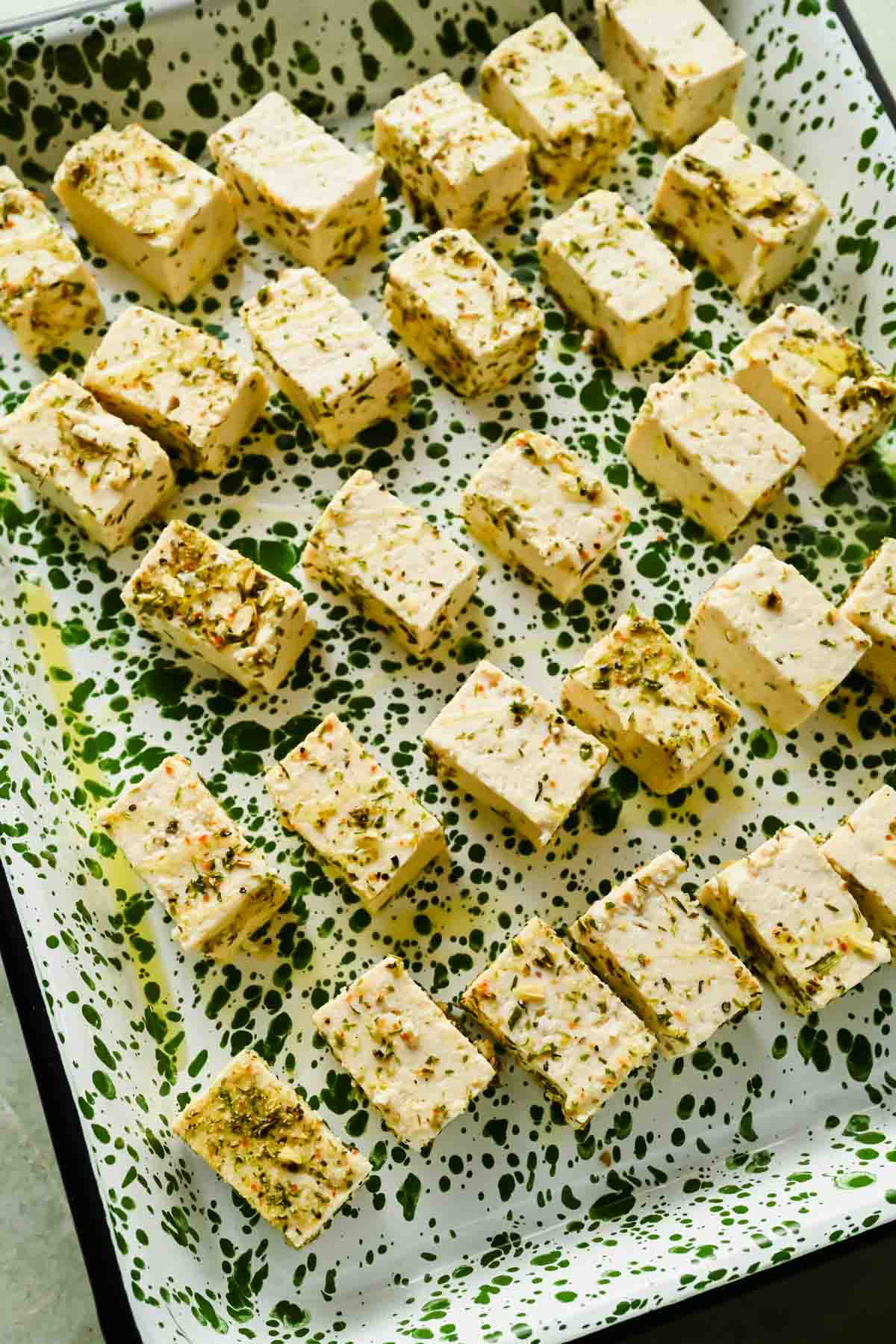 diced blocks of herbed tofu on speckled sheet pan.