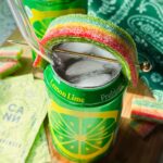 open canned cocktail garnished with airhead extreme shaped like a rainbow on a wood cutting board.