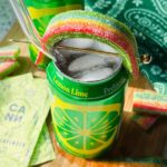 open canned cocktail garnished with airhead extreme shaped like a rainbow on a wood cutting board.
