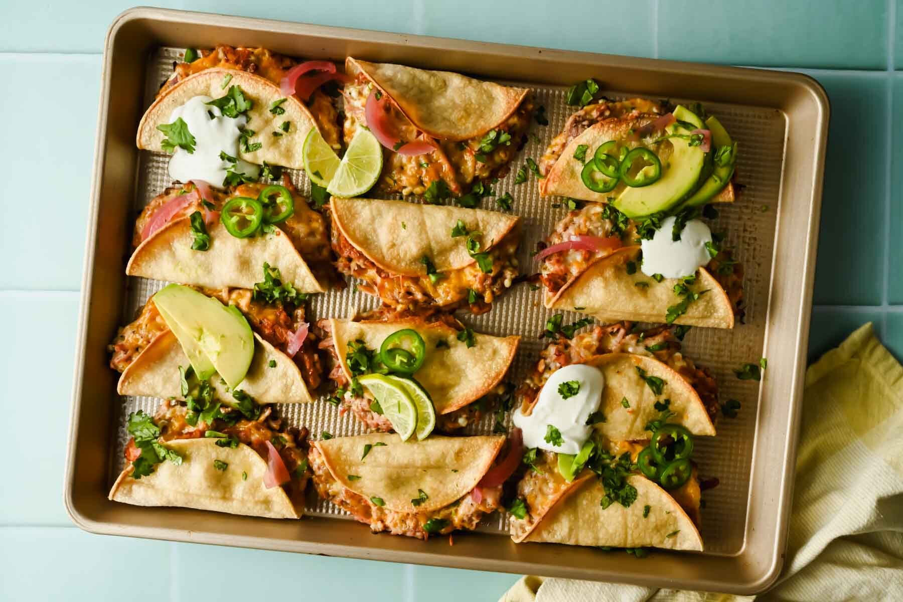 baked crispy pork tacos topped with herbs, lime wedges, avocado and sour cream.