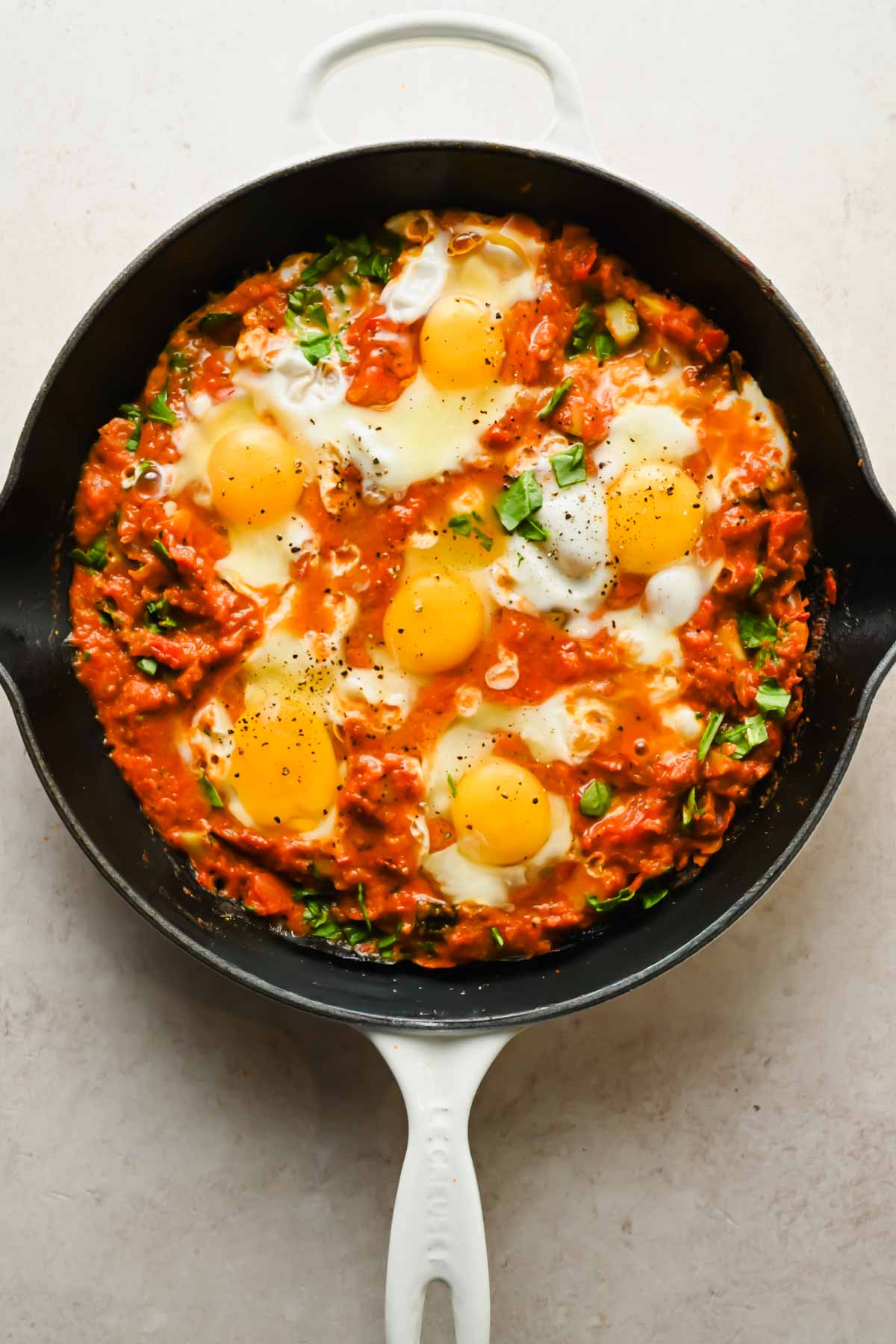 diced veggies and thick tomato sauce spread across cast iron skillet with 6 eggs cracked into pan and topped with fresh basil.