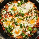 vegetarian shakshuka topped with chopped fresh herbs and feta in cast iron skillet.
