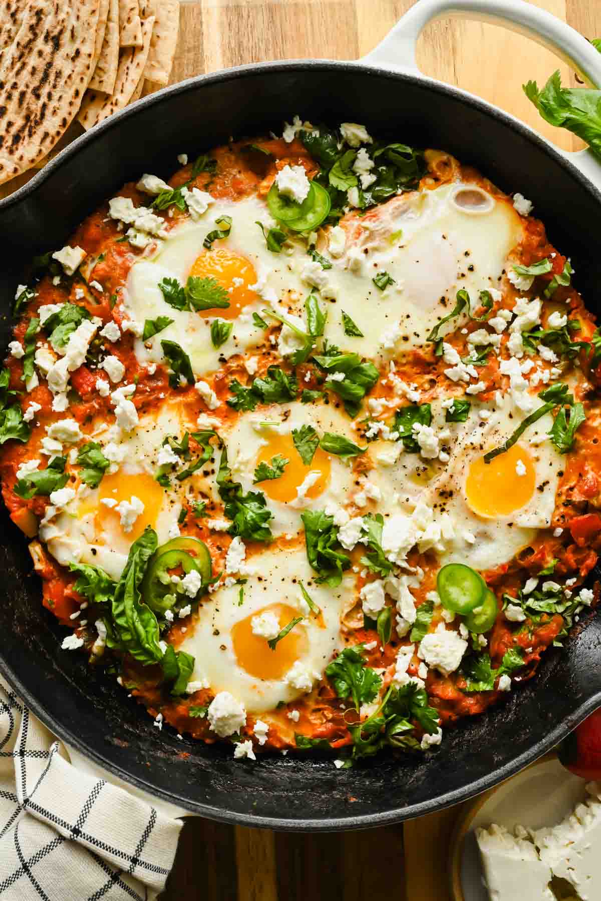 vegetarian shakshuka topped with chopped fresh herbs and feta in cast iron skillet.