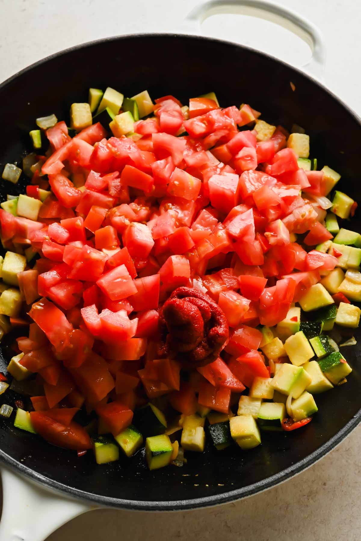 diced vegetables including zucchini, onion, and bell peppers in large cast iron skillet.