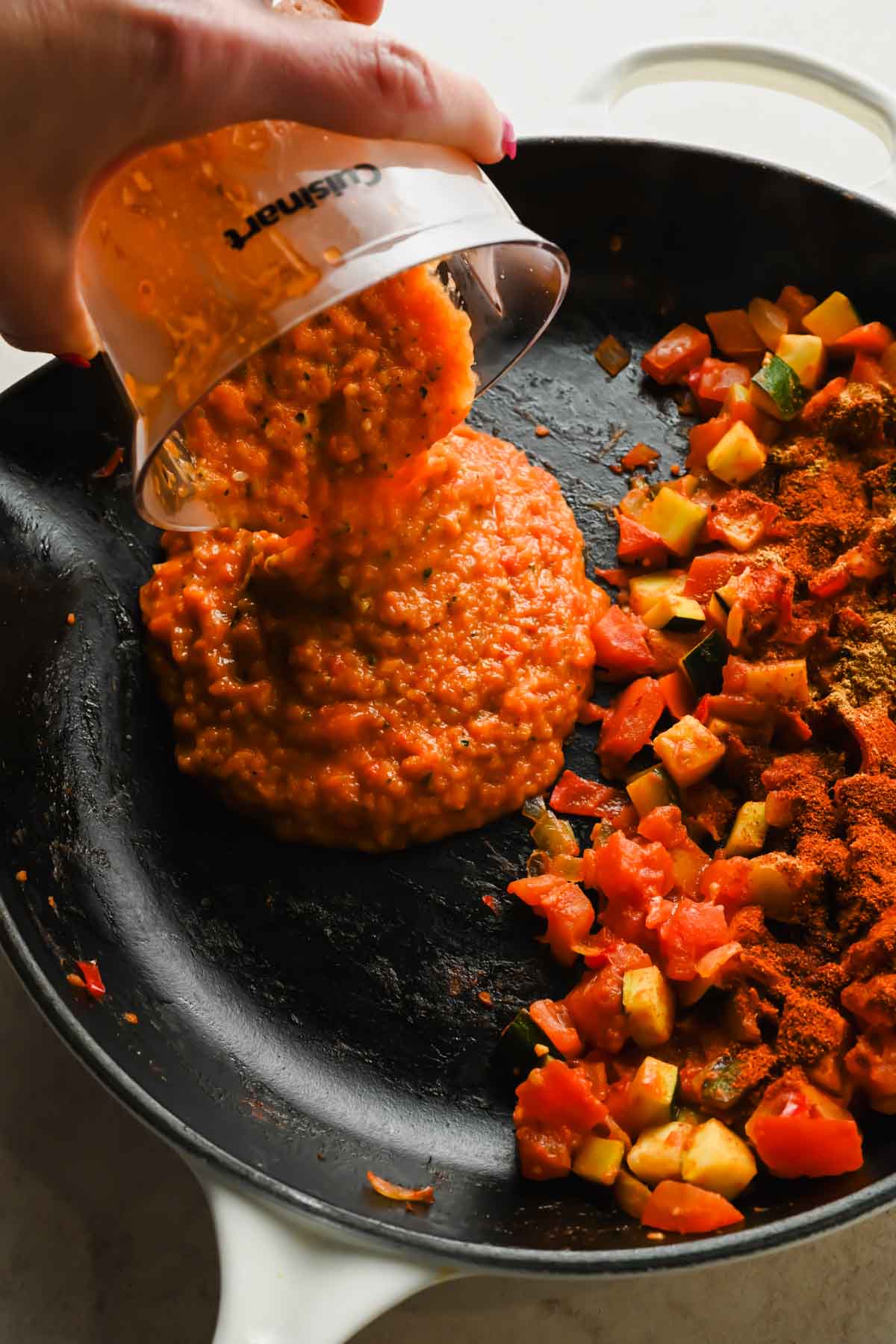 tomato sauce being poured into cast iron skillet with cooked veggies.