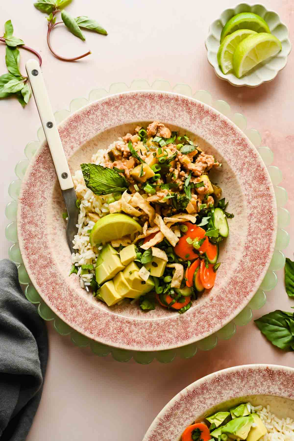 lamb stir fry in speckled bowl served over rice, garnished with avocado, green onion, herbs and veggies.