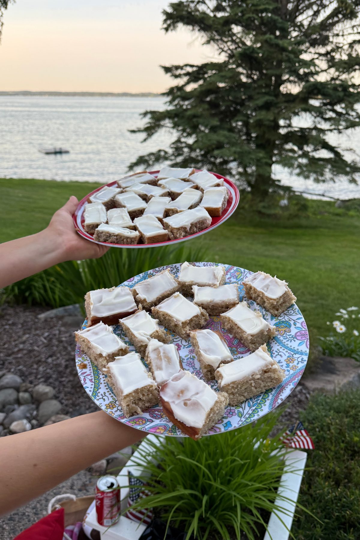 two plates side by side with pieces of banana cake squares overlooking a lake and pine tree in the background.
