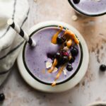 wild blueberry smoothie in glass with striped straw garnished with blueberries, peanut butter, and oat flakes.