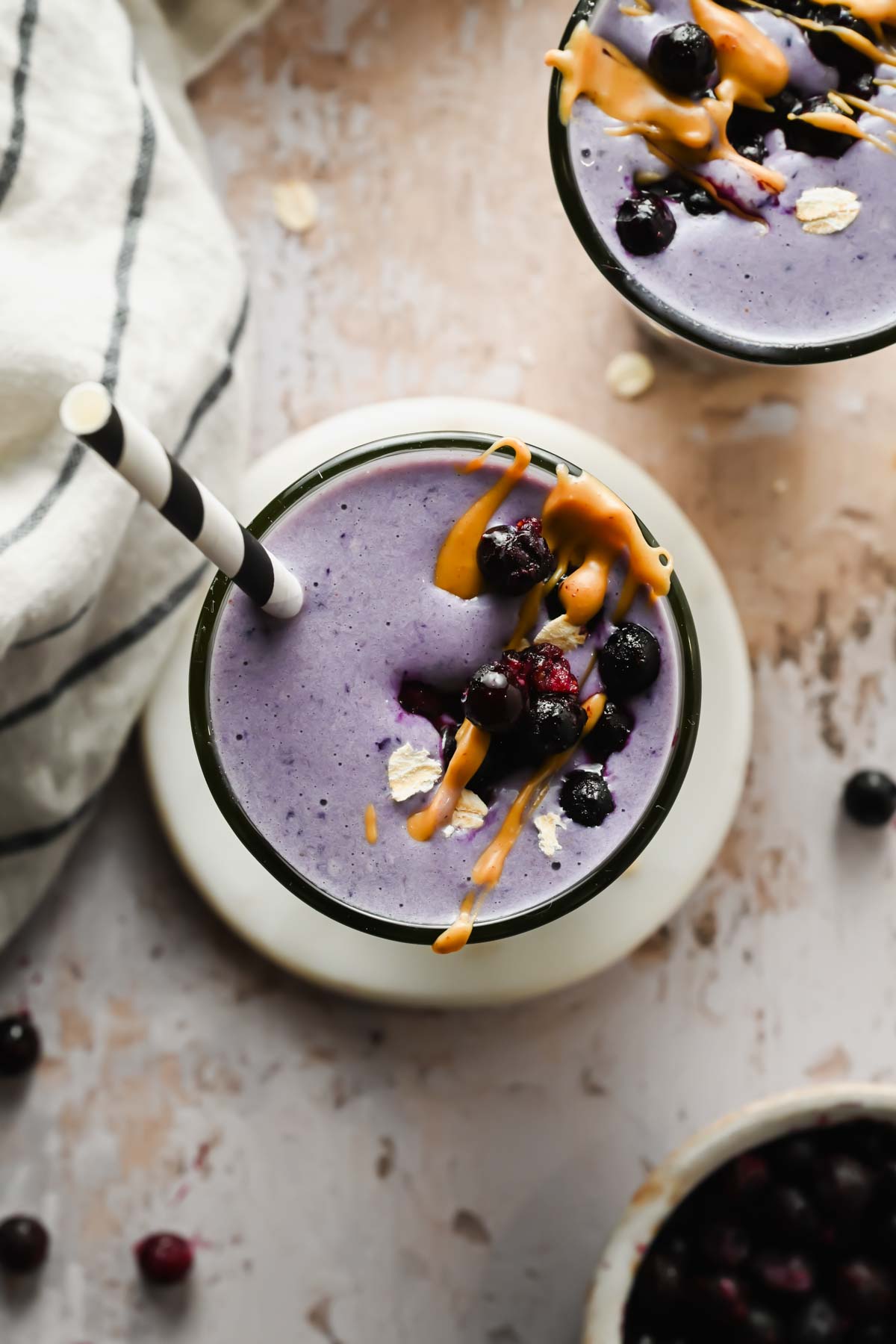 wild blueberry smoothie in glass with striped straw garnished with blueberries, peanut butter, and oat flakes.
