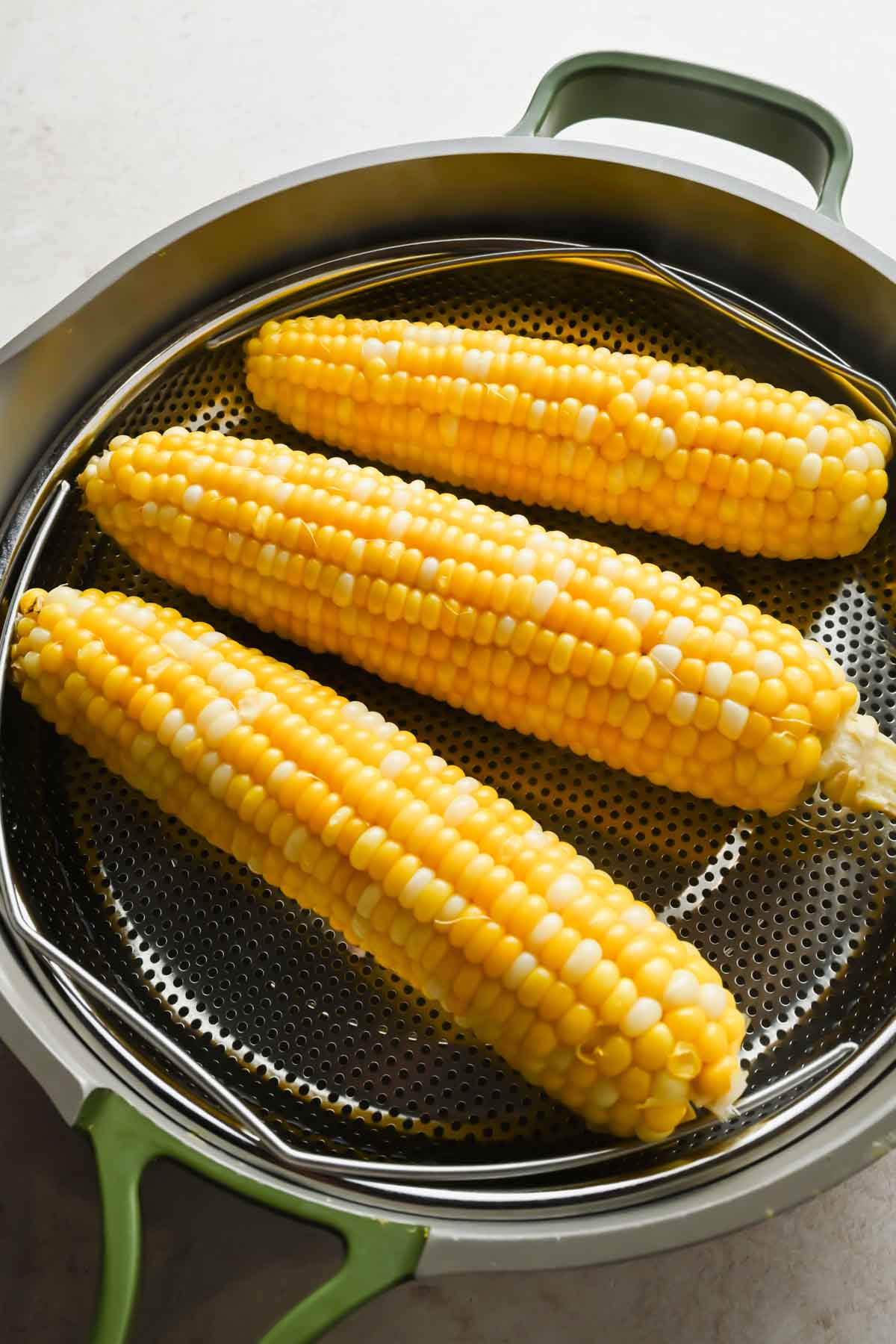 three corn on the cob pieces in steamer basket in large skillet.