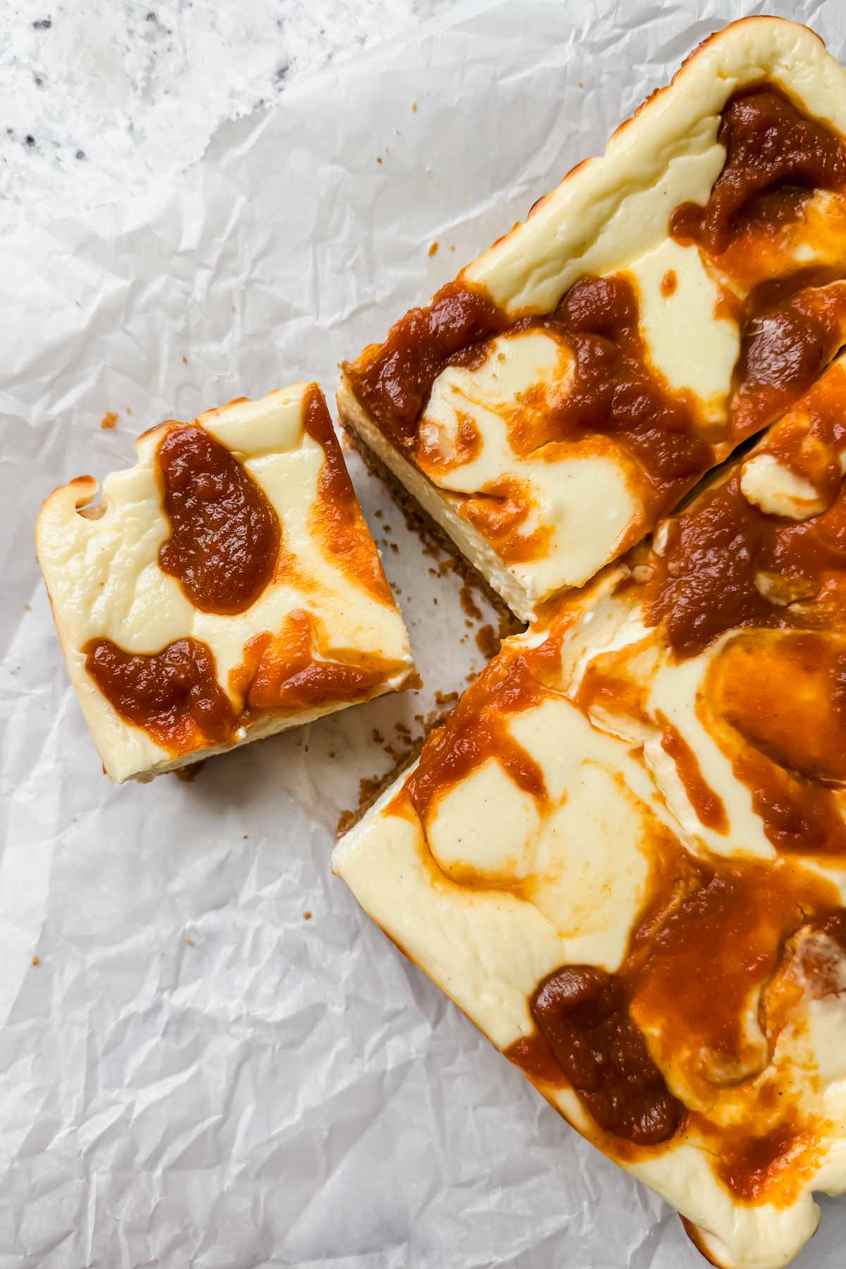 Squares of protein cheesecake bars with pumpkin butter swirl on parchment.