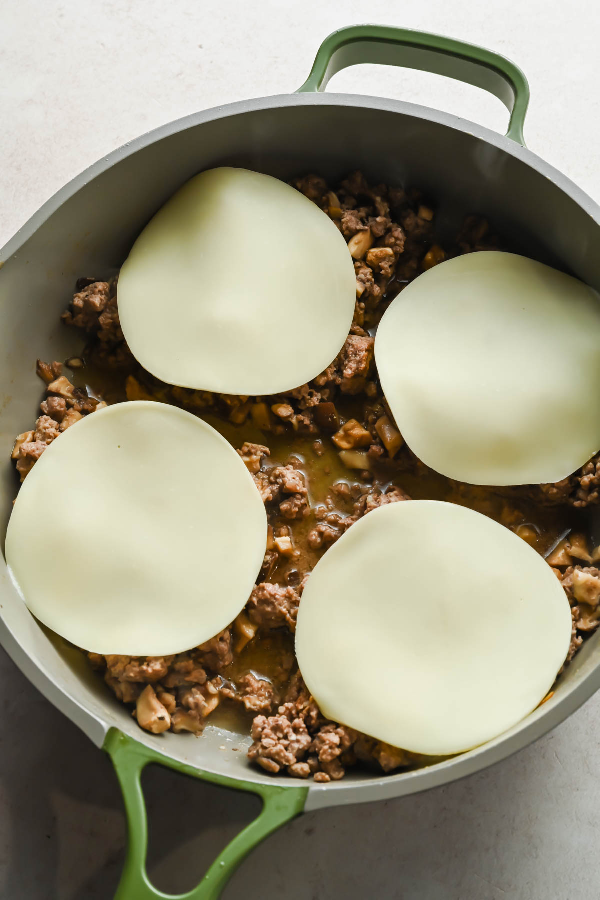 ground beef topped with slices of provolone cheese in large skillet.