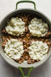 ground beef topped with slices of melted provolone cheese in large skillet.