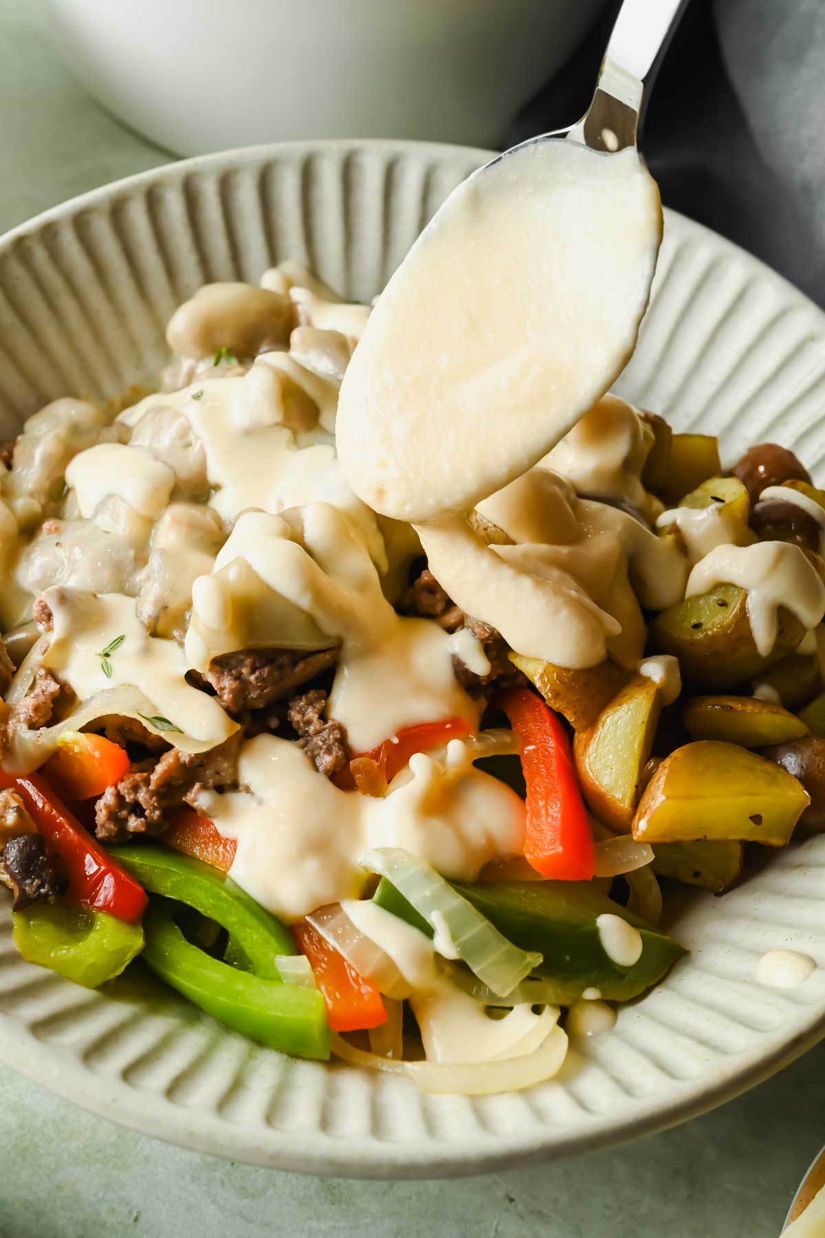 Philly cheesesteak bowl being drizzled with sauce in white serving dish.