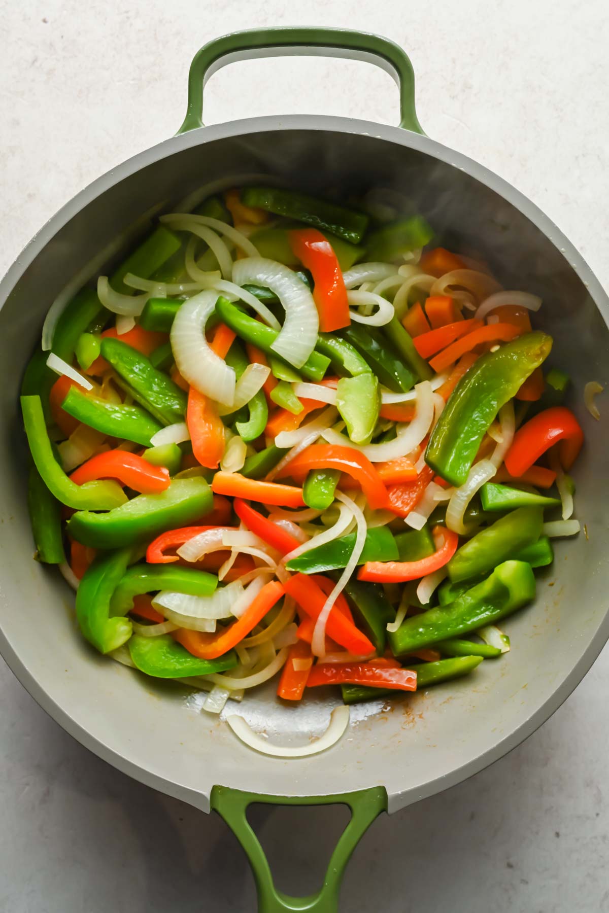 sliced bell peppers and onions cooking in large skillet.