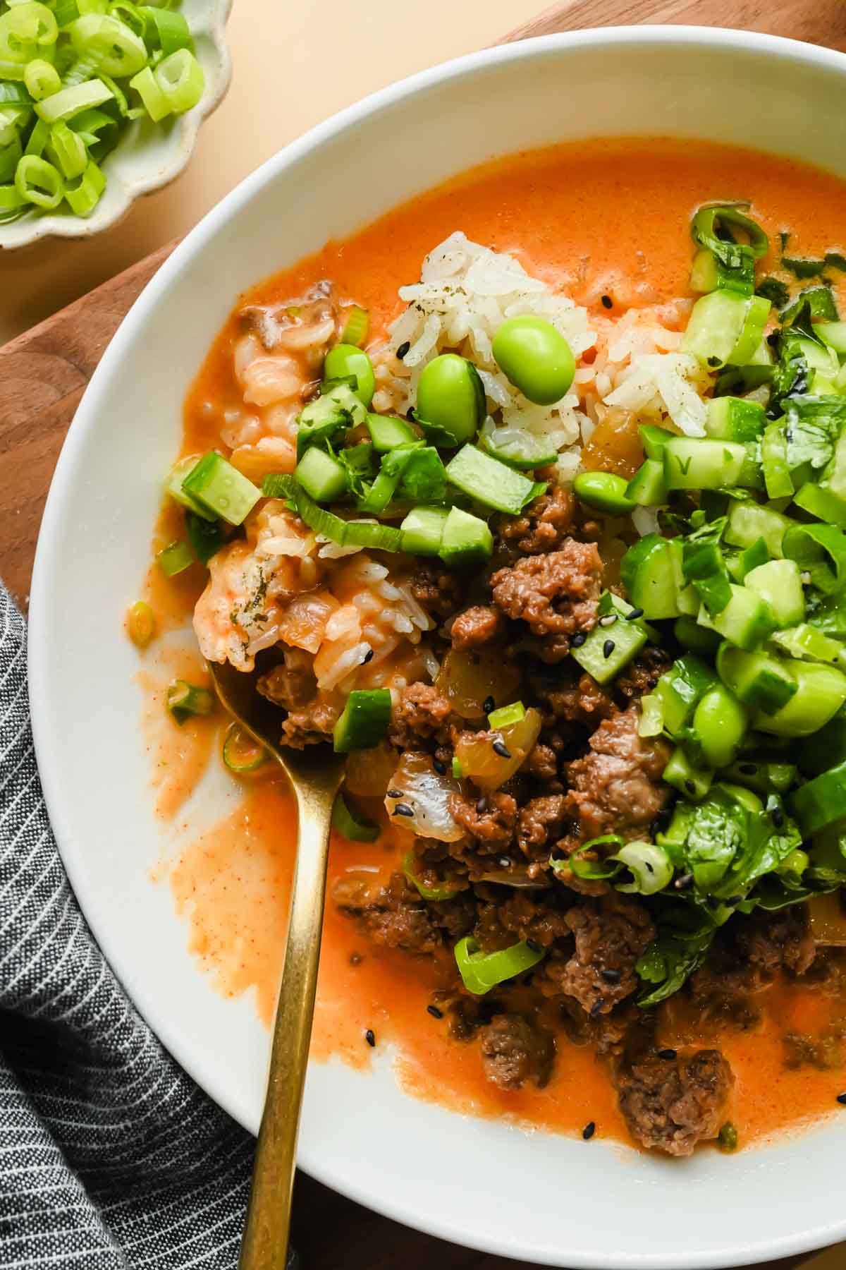 ground beef coconut rice bowl topped with edamame and fresh herbs in white serving dish with gold spoon.