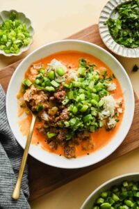 ground beef coconut rice bowl topped with edamame and fresh herbs in white serving dish with gold spoon.